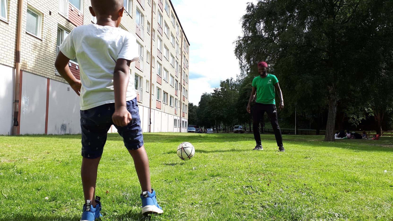 Ett barn och en områdesvärd som spelar fotboll i Växjö stad